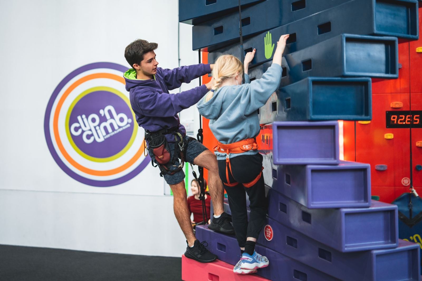 An instructor shows a child how to climb an indoor climbing wall